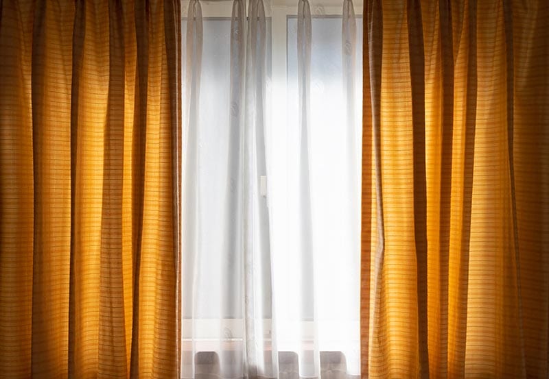 A brightly backlit window framed by layered drapes.