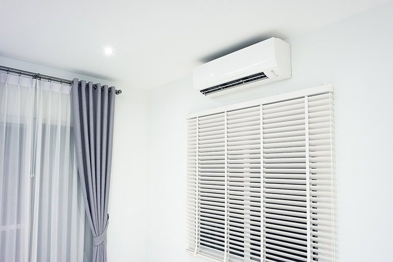 A white mini-split air conditioning unit mounted high on a plain white wall inside a modern room.