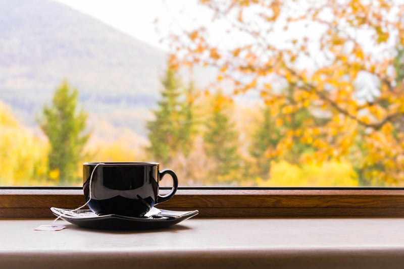 A black teacup and matching saucer sitting on a windowsill, with a tea bag string hanging over the side of the cup.