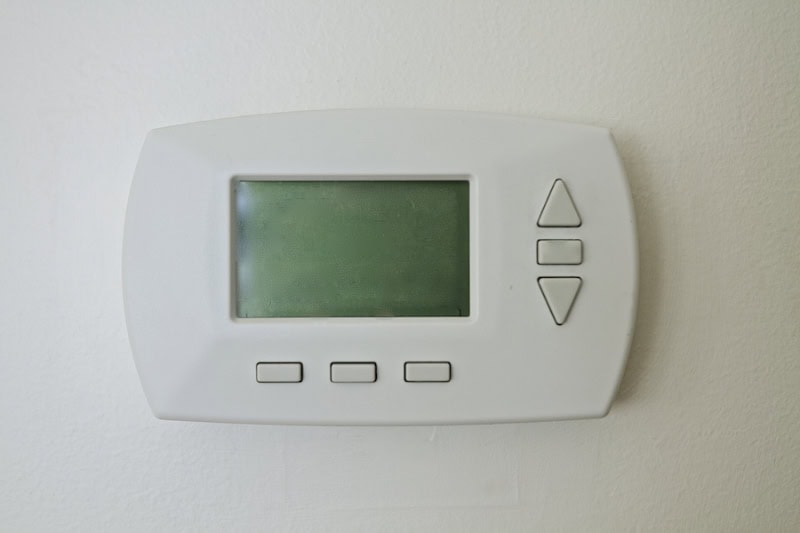 Photo of a digital thermostat mounted on a wall with a blank screen.